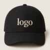 Black curved-brim cap with embroidered “logo” text in white on the front pane