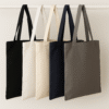 Five canvas tote bags in black, white, natural, navy, and mushroom colors hanging neatly on a white wooden rod against a neutral background