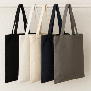 Five canvas tote bags in black, white, natural, navy, and mushroom colors hanging neatly on a white wooden rod against a neutral background
